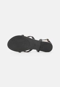 Black strappy sandal featuring a textured flat sole, adjustable ankle strap with metal buckle, and minimalistic design.