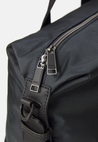 Geantă din nylon negru cu o suprafață texturată, având fermoare și accesorii argintii. Include o curea detașabilă pentru versatilitate.