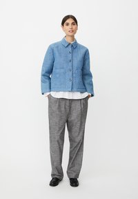 Blå quiltet jakke med knaplukning foran, med geometriske mønstre; kombineret med grå ternede bukser og sorte sko.