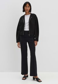 Giacca nera corta con zip argentata, top bianco aderente, pantaloni a palazzo scuri e scarpe scivolate nere. Tessuto liscio, design minimalista.