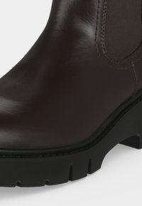 Bottine en cuir marron foncé avec panneau latéral élastique et talon épais à semelle crantée noire.