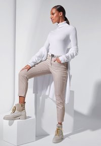 Witte geribbelde coltrui, beige gestreepte tapered broek en chunky beige laarzen met gouden veters. Model poseert op een pootje tegen een neutrale achtergrond.