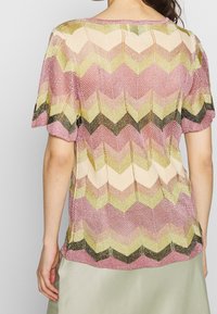 Short-sleeve top featuring a chevron pattern in pink, gold, green, and black, with a textured knit fabric and a round neckline.