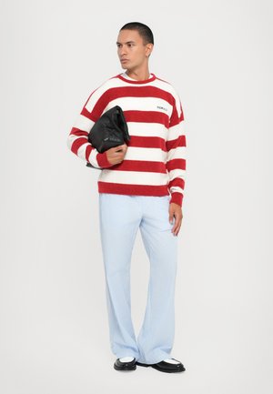 Pull rayé rouge et blanc, coupe décontractée, avec le logo "Fiorucci". Associé à un pantalon rayé bleu clair et un sac noir, chaussures à bouts pointus.