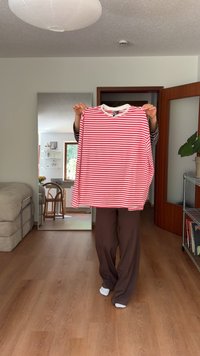 Red and white striped long-sleeve shirt with a round neck and a relaxed fit, held up in a room with wooden flooring and a mirror.