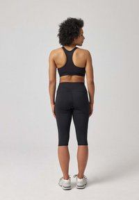 Zwarte sportieve crop top en high-waisted capri legging, slim fit ontwerp, rekbare stof, gecombineerd met witte sportieve schoenen, minimalistische stijl.