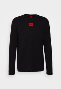 Schwarzes langärmliges T-Shirt aus Baumwolle mit einer roten quadratischen Applikation, die den Text "HUGO" zentral auf der Brust zeigt. Rundhalsausschnitt und normale Passform.