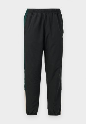 Pantalons de sport noirs avec une taille élastique, présentant des panneaux latéraux verts et beiges et un design de jambe fuselée. Fabriqués en matériau léger.