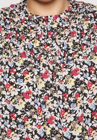 Kukkakuosiset puserot mustalla taustalla, jossa on pieniä punaisia, keltaisia ja sinisiä kukkia. Teksturoitu kangas, jossa on rypytetty pääntie ja laskokset.