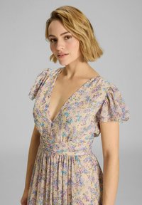 Blumenkleid in hellbeige mit lila und blauen Mustern, V-Ausschnitt, kurzen puffigen Ärmeln und fließendem Rock. Weicher, leichter Stoff.