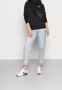 Svart hoodie med hög krage, ljusblå slitna jeans och vita Nike Air Max sneakers med marinblå detaljer. Svart axelväska.