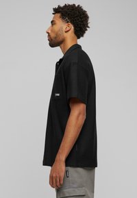 Black short-sleeve polo shirt with a textured fabric, collar, and single chest pocket displaying a small logo.