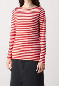 Langærmet bluse med røde og cremefarvede vandrette striber, rund halsudskæring og blød tekstur, parret med en sort denimnederdel.