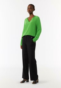 Green v-neck long-sleeve top paired with black wide-leg trousers and black heeled sandals. Smooth fabric with a relaxed fit.