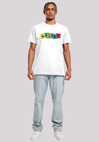 Balta trumpa rankovė t-shirt marškiniai su spalvingų periodinės lentelės kvadratų grafika raudonai, geltonai, žaliai ir mėlynai. Džinsai ir balti kedai.