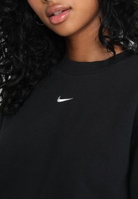 Zwarte katoenen sweatshirt met ronde hals, voorzien van een klein wit Nike-logo op de borst. Zachte textuur en een relaxte pasvorm.