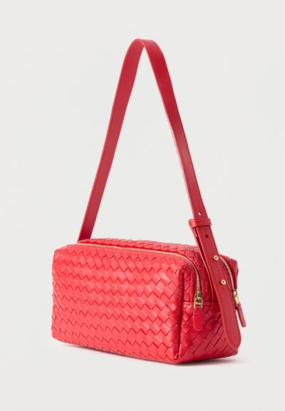 Κόκκινη ορθογώνια χειροποίητη τσάντα από δέρμα με ρυθμιζόμενο ιμάντα ώμου και δύο χρυσά φερμουάρ σε λευκό φόντο.