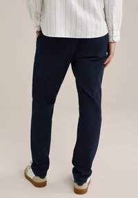 Jūras spēku sporta bikses ar teksturētu audumu, iešūtām kabatām, ar nedaudz elastīgu piegriezumu un sašaurinātu fit. Kombinētas ar ikdienišķiem apaviem, redzams aizmugurējais skats.