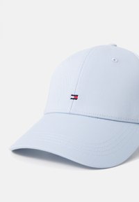 Cappellino da baseball blu chiaro in tessuto con visiera curvata. Presenta un logo ricamato rosso, bianco e blu sul davanti. Superficie strutturata.