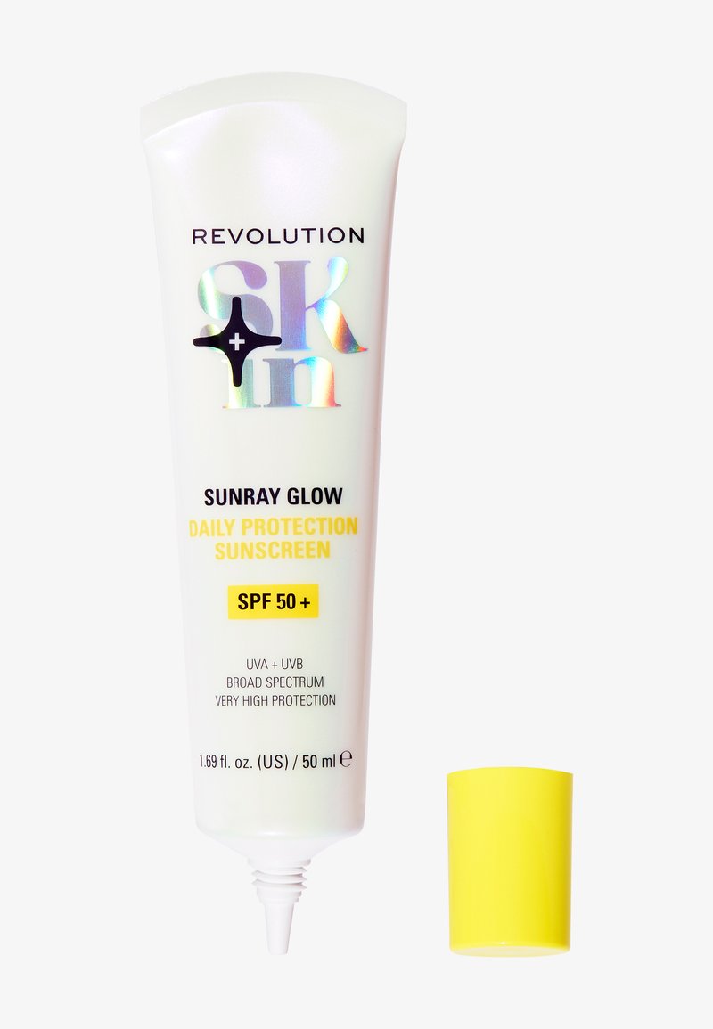 Tube de crème solaire avec un corps blanc et un texte holographique "Revolution Skin". Capuchon jaune. Le texte indique SPF 50+, protection UVA/UVB, taille de 50 ml.
