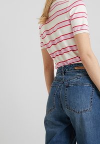 Maglietta a maniche corte a righe bianche con righe rosse, abbinata a jeans in denim blu a vita alta con due tasche posteriori e un'etichetta in pelle.