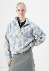 Fleece pullover in lichtblauw en crème met geometrische patronen, half-rits kraag, relaxte pasvorm en zacht, textuur materiaal.