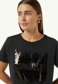 Black t-shirt featuring a "SPARKLE" graphic in varying sequins, creating a textured, shiny pattern. Short sleeves and round neck design.