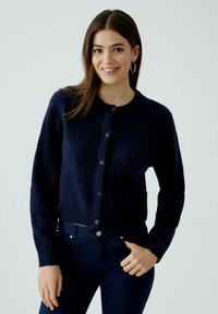 Marineblauer, gestrickter Cardigan mit Rundhalsausschnitt, langen Ärmeln und Knopfleiste. Weicher Stoff mit gerippten Akzenten und stoffbezogenen Knöpfen.