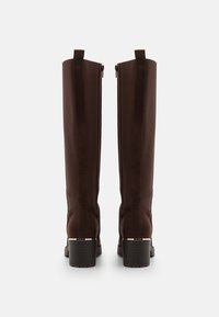 Bottes hautes marron en daim et mélange de tissu. Dotées d'un bout arrondi, d'une fermeture éclair et d'un talon épais. Texture lisse, couleur unie.
