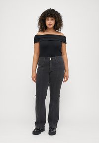 Svart off-shoulder bodysuit i kombination med högmidjade, mörkgrå jeans. Jeansen har två knappar fram och synliga sömdetaljer.