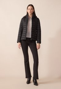 Svart boblejakke med horisontalt quilted design, glidelås foran og hette. Kombinert med grå topp og svarte vide jeans, brukt med svarte støvler.