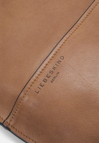 Cuir tan avec une surface texturée, présentant une ligne de couture sombre et le nom de marque embossé "LIEBESKIND BERLIN." Détails à finition lisse.
