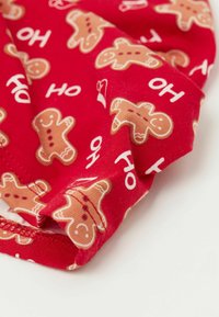 Červená látka s opakujícím se vzorem perníčků a textem "HO". Látka má měkkou texturu s přizpůsobeným šitím.