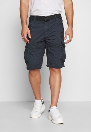 Marineblauwe cargoshorts met meerdere zakken en gestikte details, gecombineerd met een zwarte riem en witte sneakers met marineblauwe accenten.
