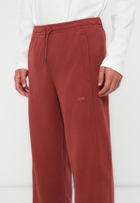 Burgunderfargede fleece joggebukser med elastisk midje, snøring og sidelommer; har et logomerke på venstre lår.