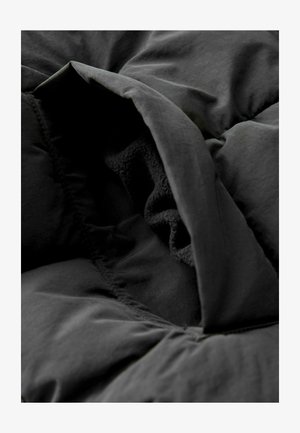 Schwarze gepolsterte Decke mit einer weichen, strukturierten Unterseite und einer glatten oberen Schicht. Verfügt über geraffte Kanten, die die Isolierung und Wärme verbessern.