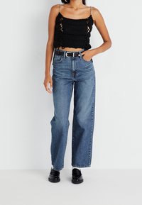 Svart stickad kort topp med silvriga kedjestraps, kombinerad med högmidjade blå denimjeans. Inkluderar ett svart bälte och svarta loafers.