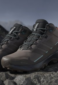 Tumma harmaat vaelluskengät, joissa on teksturoitu verkkopinta, vahvistettu kärki ja turkoosit yksityiskohdat. Varusteena vedenpitävä Gore-Tex-materiaali.