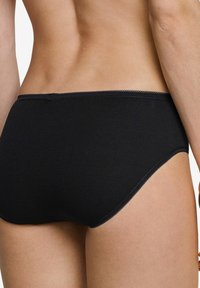 Nahaufnahme des unteren Rückens und der Hüften einer Person, die schwarze, nahtlose, hochgeschnittene Unterwäsche mit gewellten Kanten trägt.