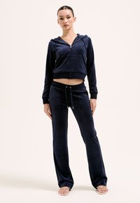 Navyblå velourträningsoverall med en zip-up hoodie med framfickor och matchande byxor med resårmidja, dragsko och sidfickor.