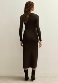 Vestito a maniche lunghe in maglia a coste di colore marrone scuro, silhouette aderente, lunghezza al ginocchio, con scollo rotondo e maniche aderenti.