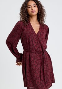 Burgundowa sukienka w stylu kopertowym z czarnym wzorem serc, długie rękawy, głęboki dekolt w serek oraz paskiem w talii. Lekki, zwiewny materiał o miękkiej teksturze.