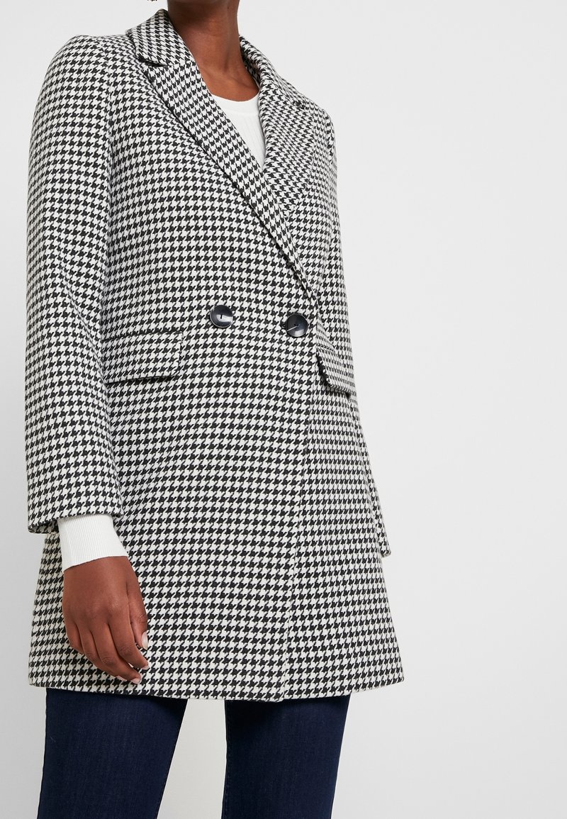 Blazer a motivo scozzese in bianco e nero, con design doppiopetto, rever a punta e due tasche frontali.