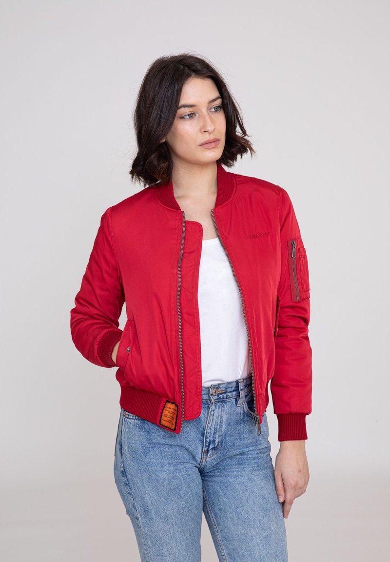 Rote Bomberjacke mit einem Reißverschluss, gerippten Bündchen und Kragen; verfügt über eine Seitentasche und eine strukturierte Oberfläche. Trägt man über einem weißen Oberteil.