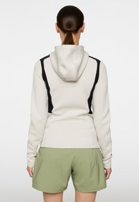 Hoodie i krämfärg med svarta detaljer, med strukturerad tyg och figursydd design, i kombination med ljusgröna shorts.