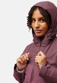 Paarse waterdichte jas met capuchon, voorzien van een ritssluiting aan de voorkant, elastische manchetten en een logo op de borst. Soepele textuur en modern ontwerp.