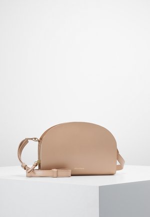 Bolso bandolera beige semicircular con correa ajustable y pequeña cremallera dorada, colocado sobre un pedestal blanco contra un fondo liso.