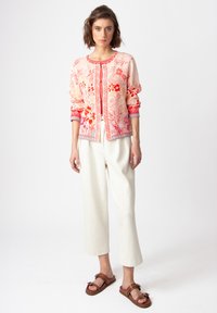 Light pink cardigan with floral prints in red and orange, featuring a round neckline and button front; paired with cream wide-leg pants.