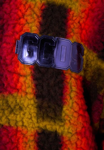 Tissu en tricot dans des tons vibrants de rouge, orange, jaune et marron avec un aspect texturé et duveteux. Comprend un patch logo noir avec l'inscription "GCDS."