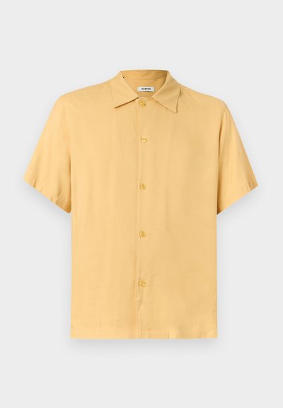 Πουκάμισο με κοντό μανίκι και κουμπιά σε ανοιχτό μουσταρδί χρώμα, με κλασικό γιακά, παρουσιασμένο σε απλό γκρι φόντο.